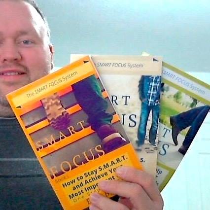 Eric Beaty playing guitar posing with Breedlove and Ibanez guitars wearing a NaNoWriMo winner shirt and posing with Smart Focus book series