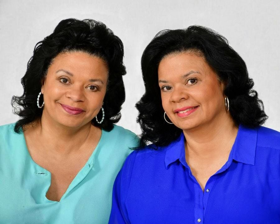 Two African American women in blue shirts and hoop earrings smile at the camera