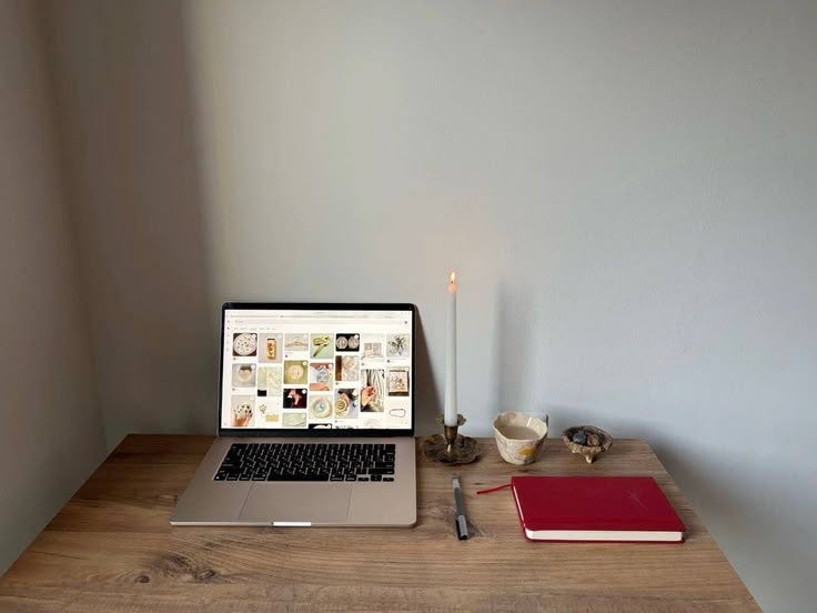 This may contain: an open laptop computer sitting on top of a wooden desk next to a candle and cup