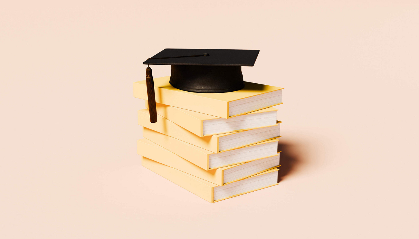 A stack of unmarked yellow books with a classic black graduation cap resting on top. (J Studios/Getty Images)
