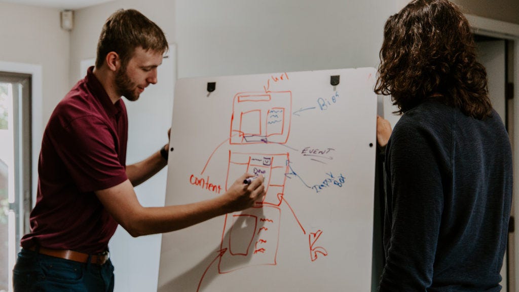 Two people standing, drawing designs on a board.