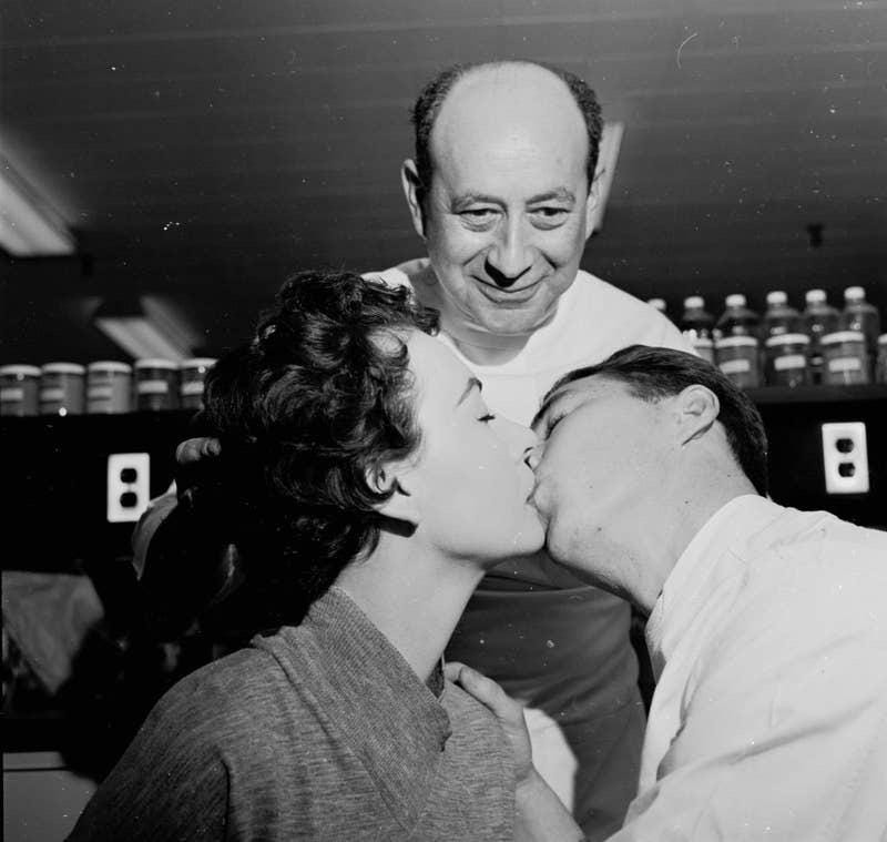 A lab technician in the 1940s observing couples kissing, a curious method used to test lipstick durability. A lab technician in the 1940s observing couples kissing, a curious method used to test lipstick durability.
