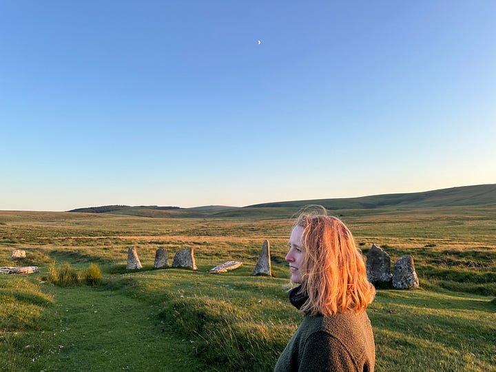 L-R: a river with rocks and trees. A white woman standing at the centre of stone circle. A hand holding a bright orange flower. A coastal path with bright green vegetation and ocean alongside it.