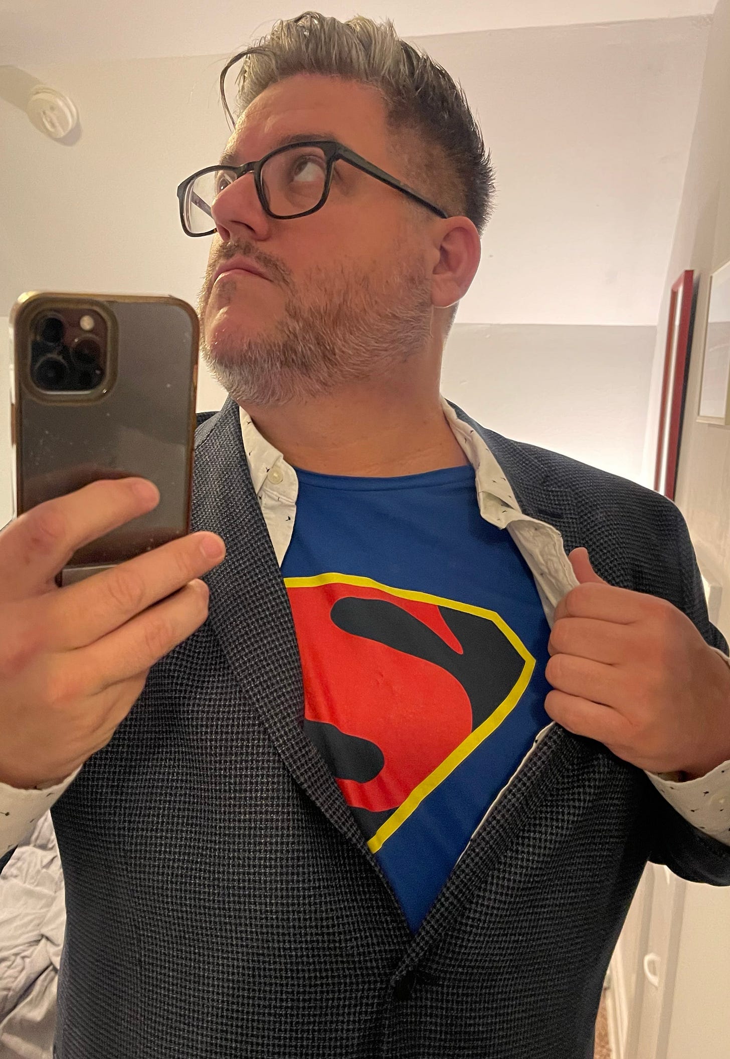 Selfie of me dressed as Clark Kent. I’m wearing a button-up shirt with a blazer, and the shirt is mostly unbuttoned to reveal a Superman logo t-shirt underneath.