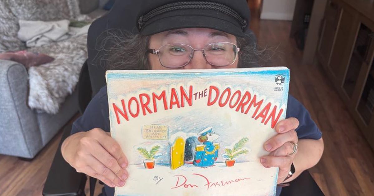 Athena holding the picture book of "Norman the Doorman" with Norman the mouse standing at attention in the snow at the mouse entrance to the art museum.