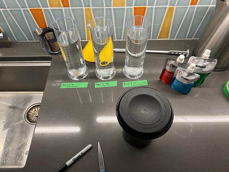 Three images. The first is a close up of a pot of chicken soup, with a ladle about to dip in. The second is a triangular bottle of Amaro Falso, and the third is a complex image with three beakers and a tank of film ready to be developed
