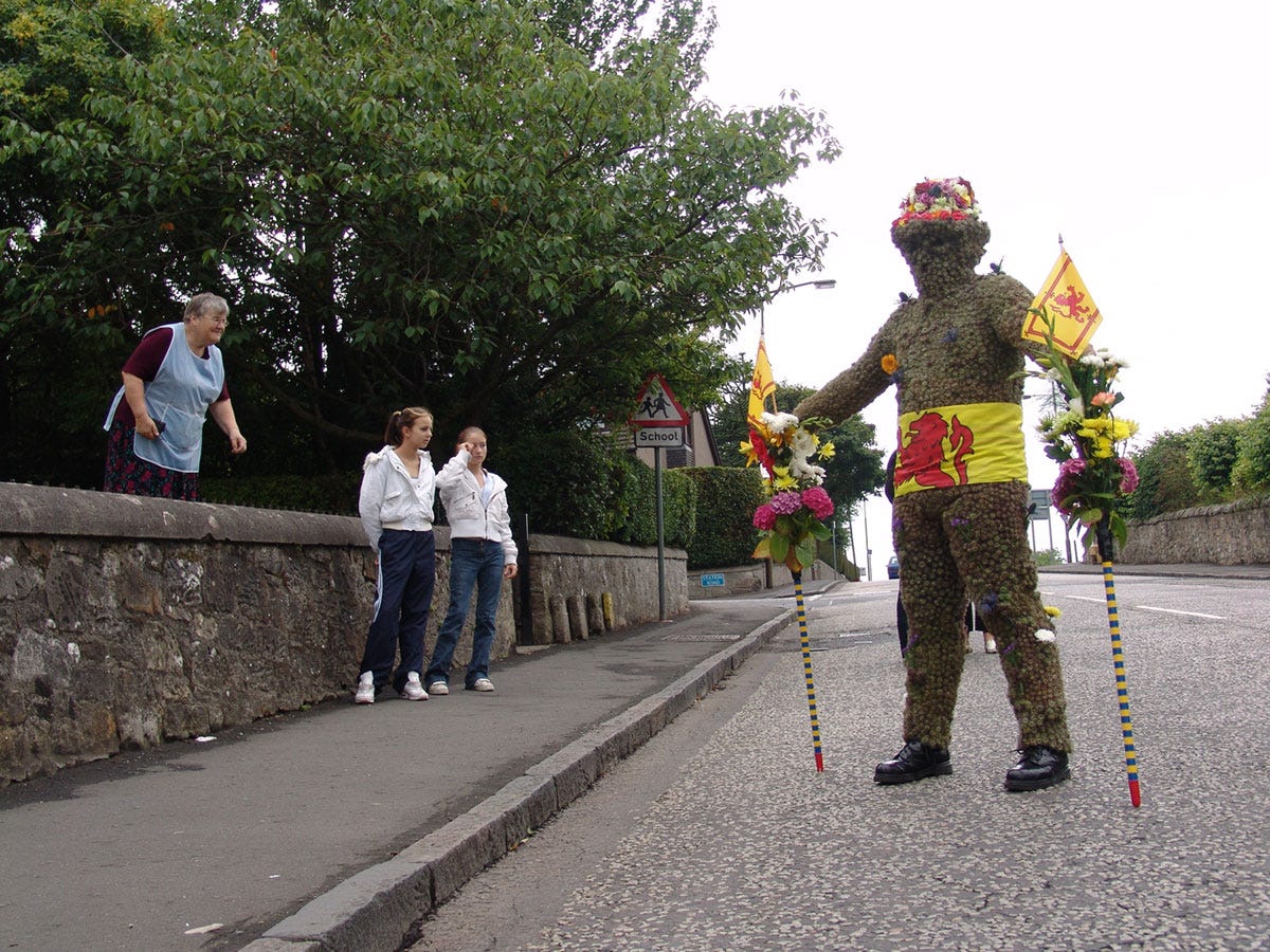 A man dressed in a prickly suit holding two poles, while three people look on A man dressed in a prickly suit holding two poles, while three people look on