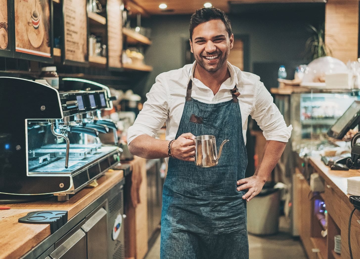 A smiling café owner standing behind the counter, representing local business collaboration in hospitality.
