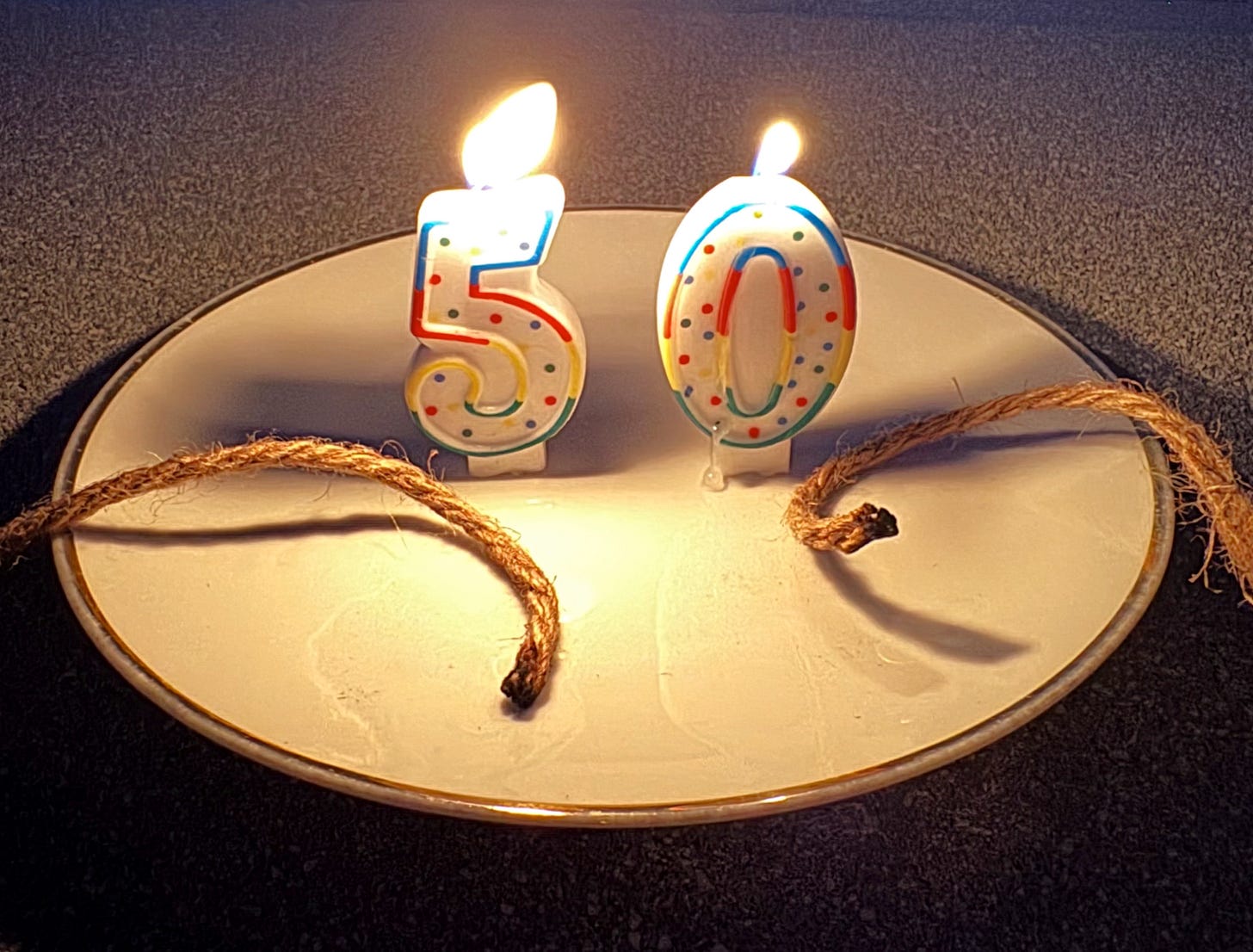 Birthday candles in the shape of the number 50 with burned cut rope ends lying in front of the candles.