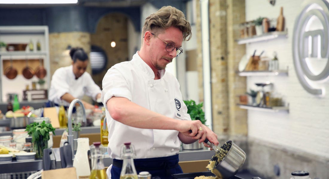 Ritchie Stainsby pouring yellow puree onto a tray with people behind him in the MasterChef kitchen