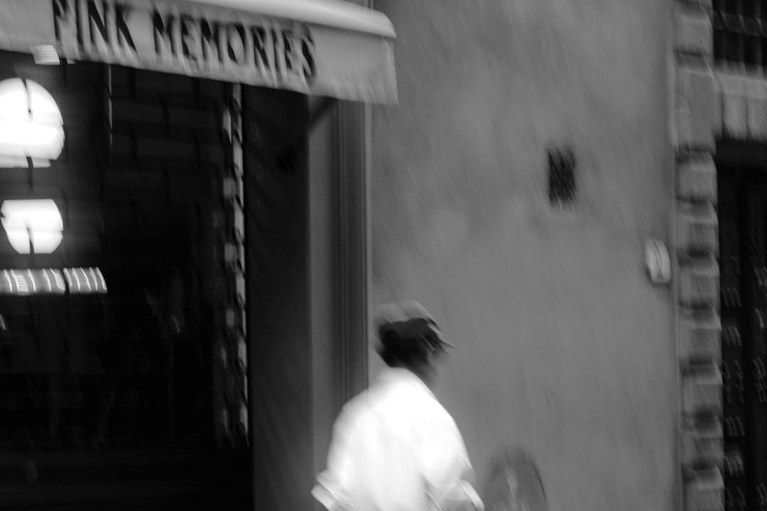 a man walking down a street past a pink store