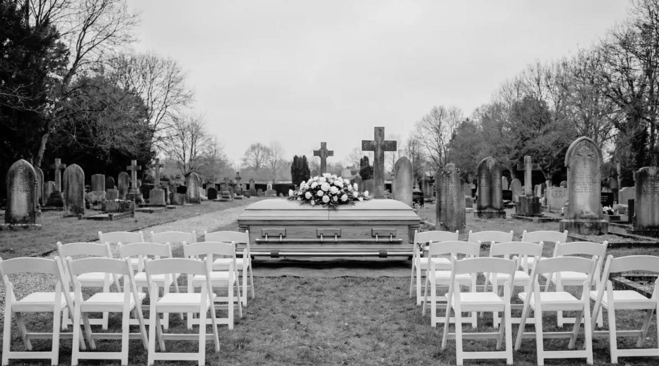 Rows of empty white folding chairs face a wooden casket in a somber black and white cemetery setting.
