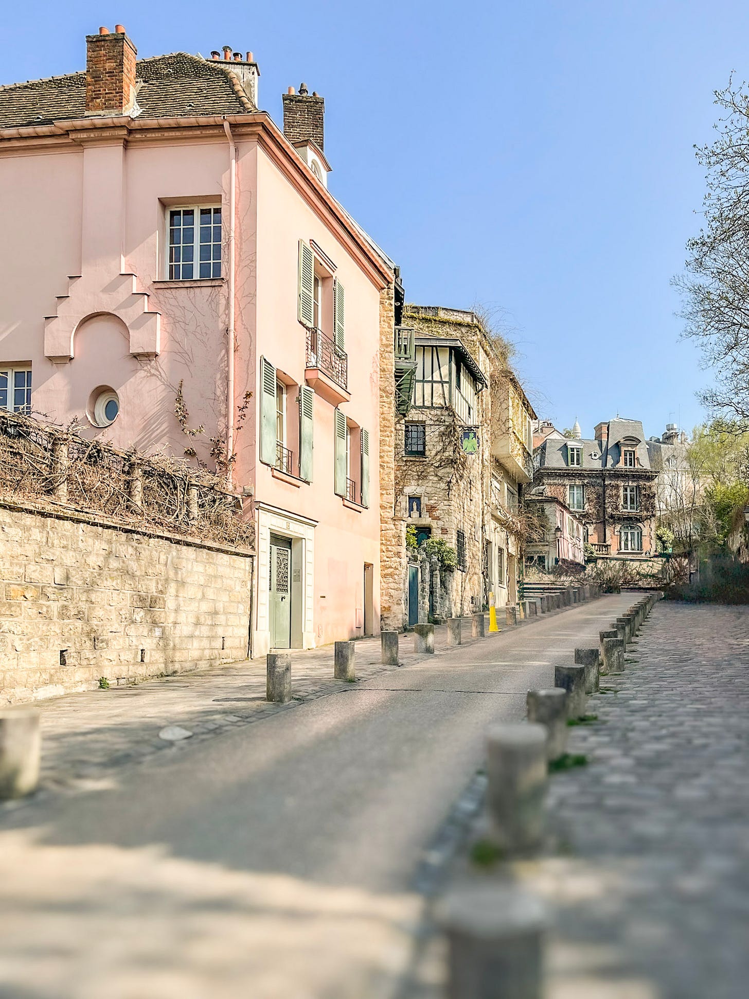Rue de l'Abreuvoir in Montmartre lined with pastel houses, cobblestones and stone façades, leading towards Sacré-Cœur in the distance.