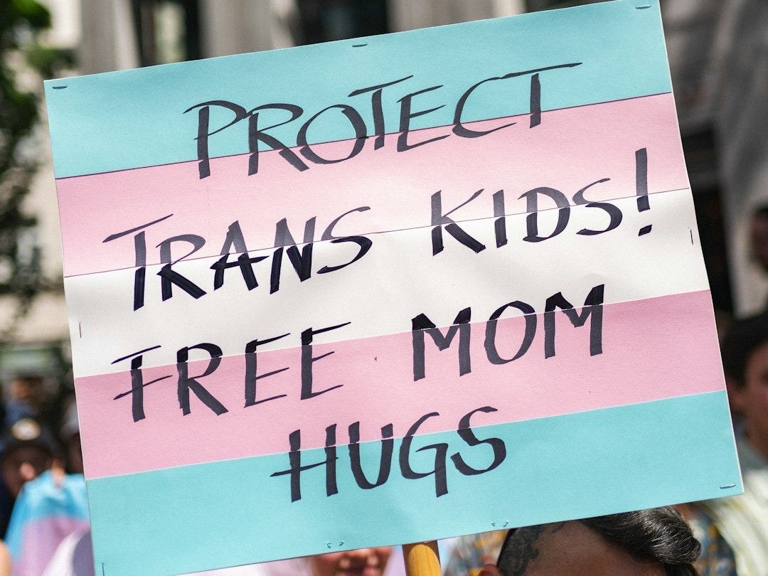 Sign at pride: protect trans kids, free mom hugs. Sign at pride: protect trans kids, free mom hugs.