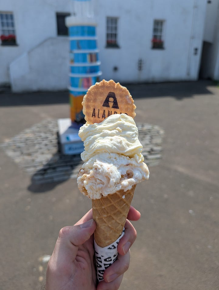 Two scoop of Alandas gelato in front of a lighthouse statue in North Berwick Lodge Gardens, then a view of the Lodge Gardens from a round wooden table