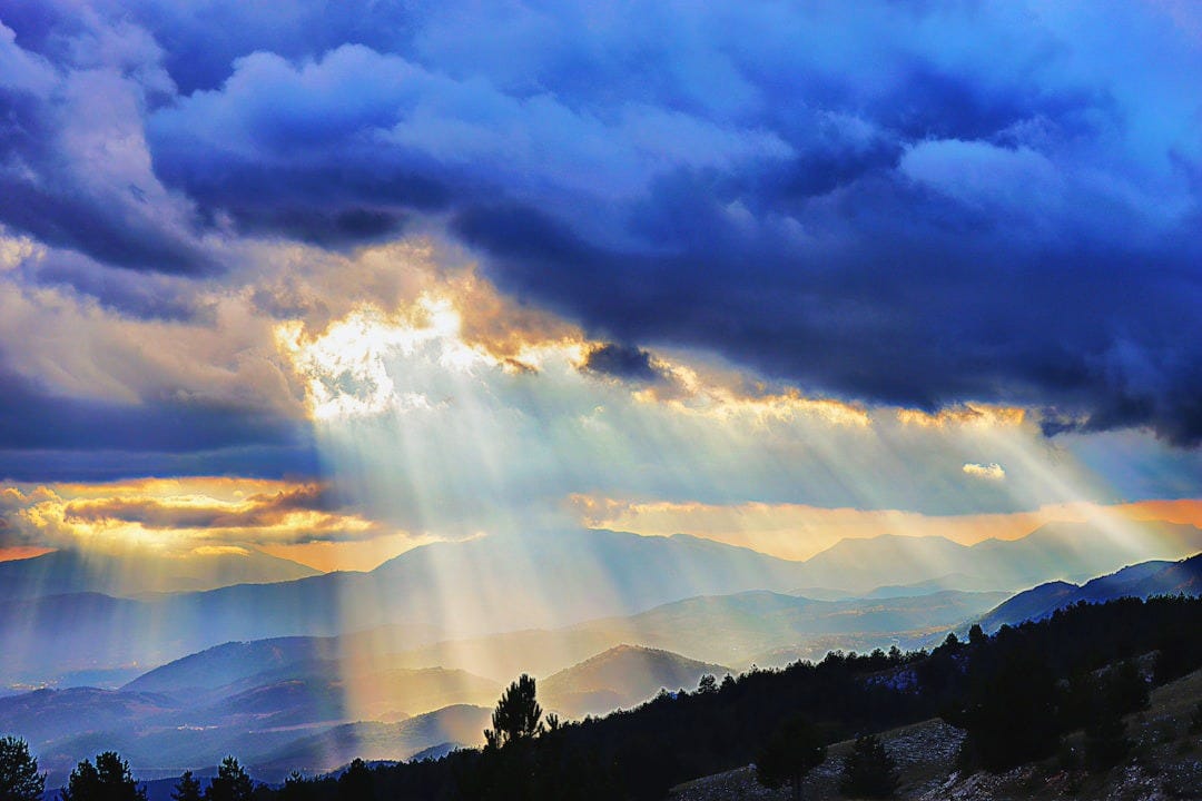 the sun rays shine through the clouds over the mountains the sun rays shine through the clouds over the mountains