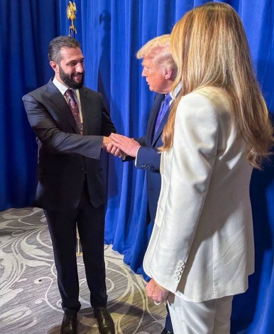 Donald Trump shaking hands with Jared Kushner. Both are dressed in suits, standing on a patterned floor with blue curtains in the background. A woman with long blonde hair, wearing a white suit, stands nearby.