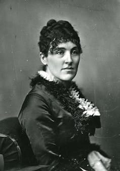 Black-and-white photographic portrait of young woman with short hair seated and posing for the camera.