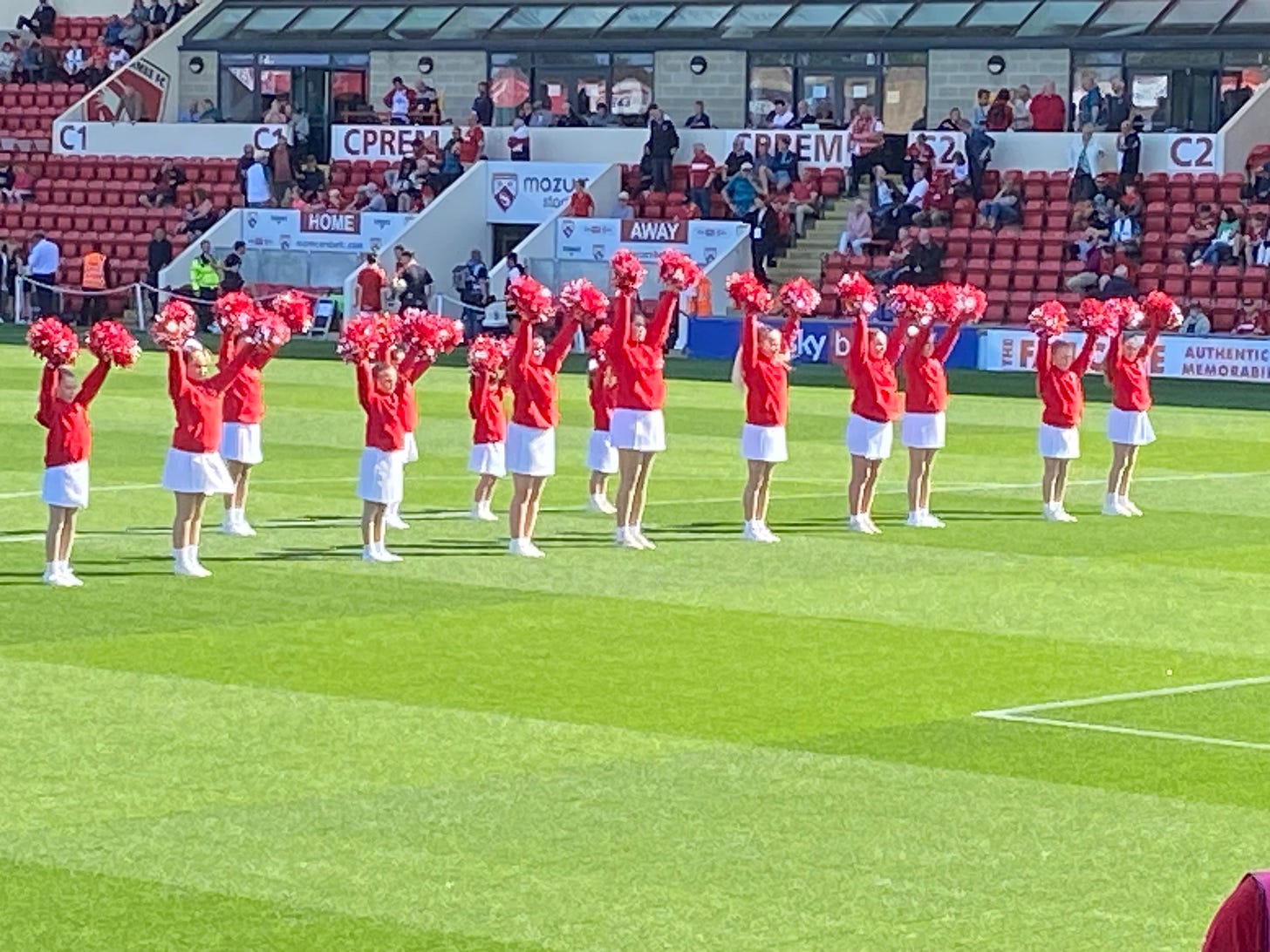 The Shrimpettes cheerleaders in action, waving their red pom-poms on a verdant pitch.