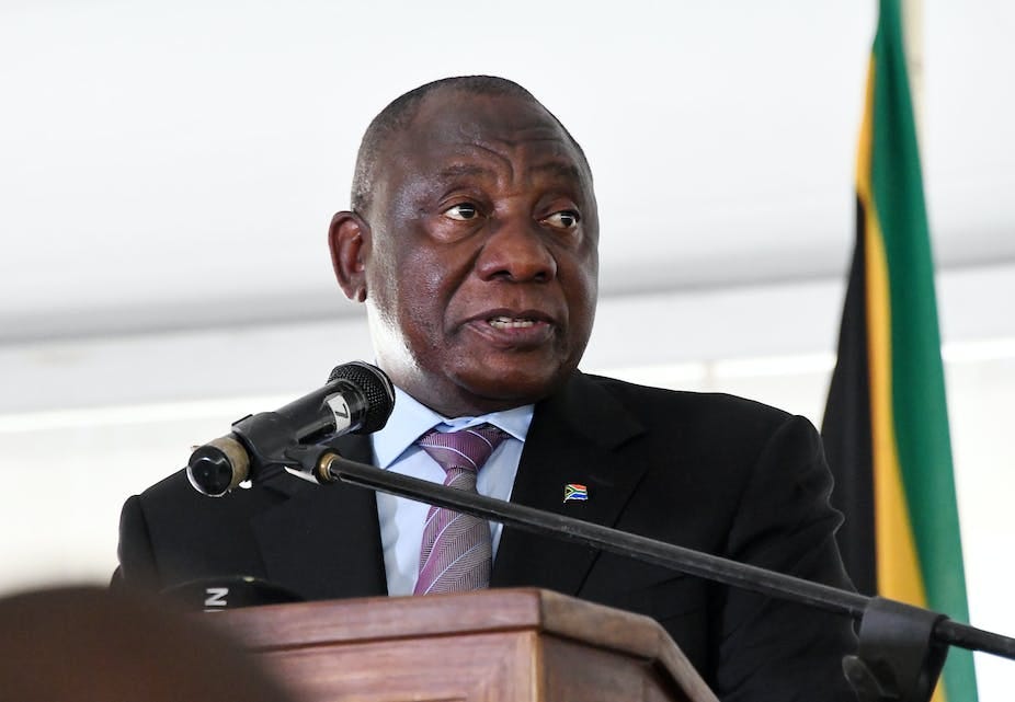 A man wearing a jacket and tie speaks into a microphone at a podium. A man wearing a jacket and tie speaks into a microphone at a podium.