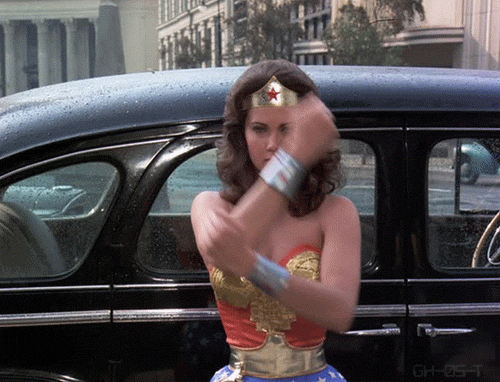 Wonder Woman, dressed in her superhero costume, strikes a pose in front of a shiny car, exuding strength and confidence. Deflecting bullets with her wrist cuffs.