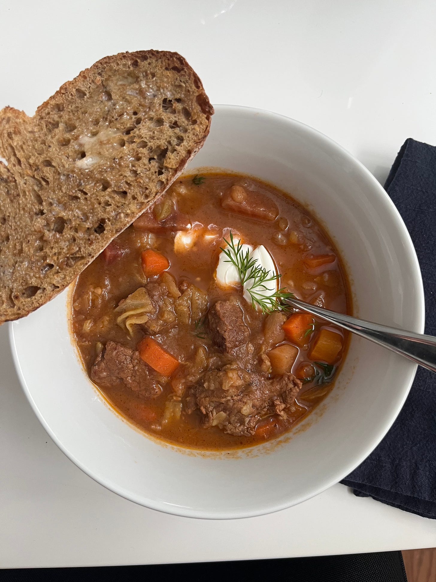 bowl of beef borscht with a slice of buttered bread balanced on top of the bowl