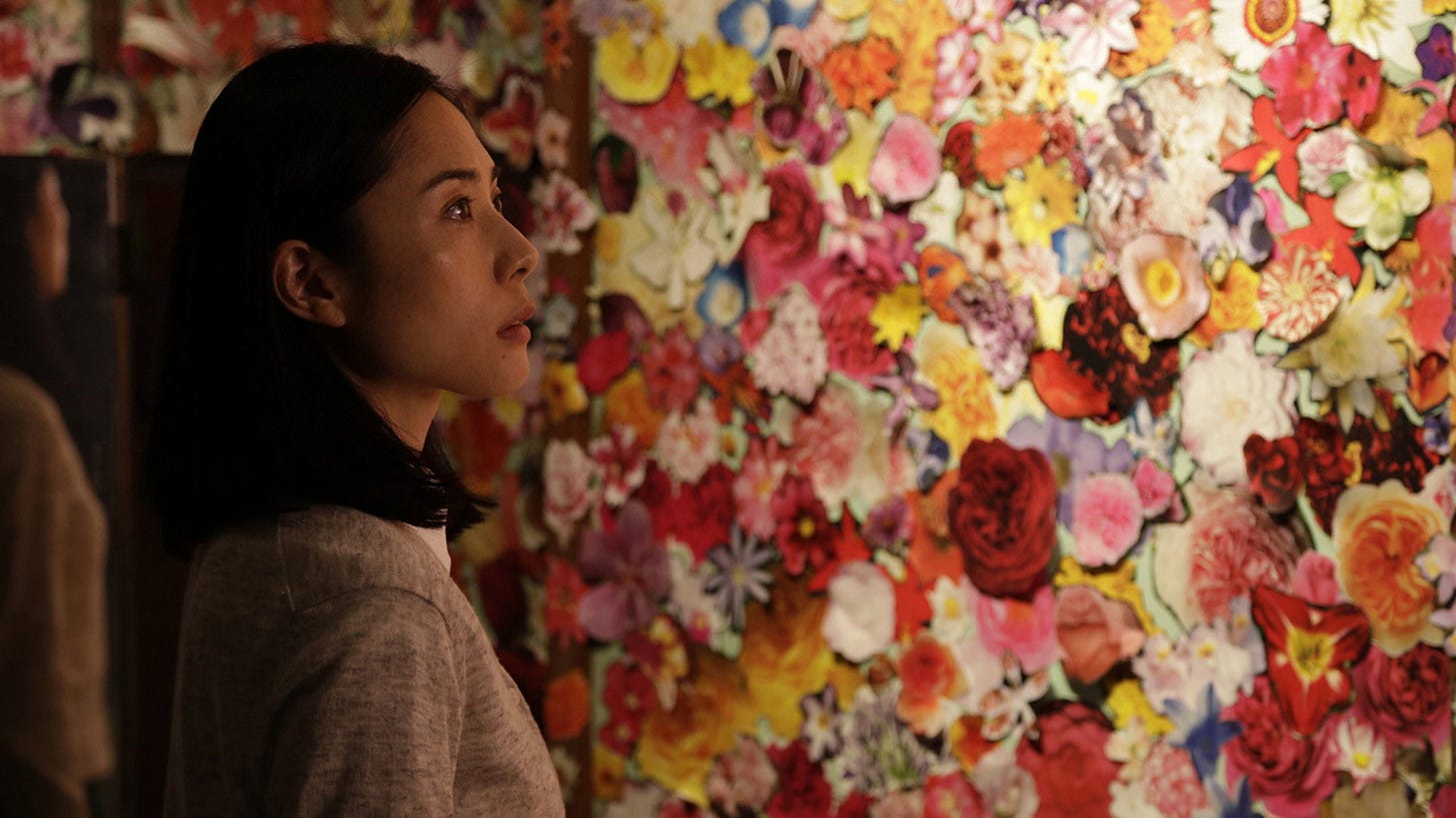 Journey to the Shore | Still features Eri Fukatsu as Mizuki looking at a wall dedicated with paper flowers.