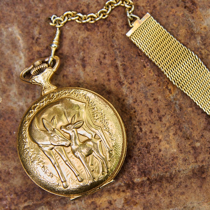 On the left is a close up of Fogel holding the watch in her hands up to her chest so we can see the detail of the woman in gold kissing a dove. On the right is a close up of the other side of the watch on a rusty background. We can see a mother and baby deer.