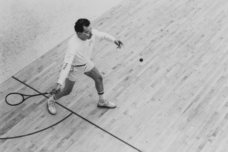 Black and white photo of man on court hitting ball with a racket