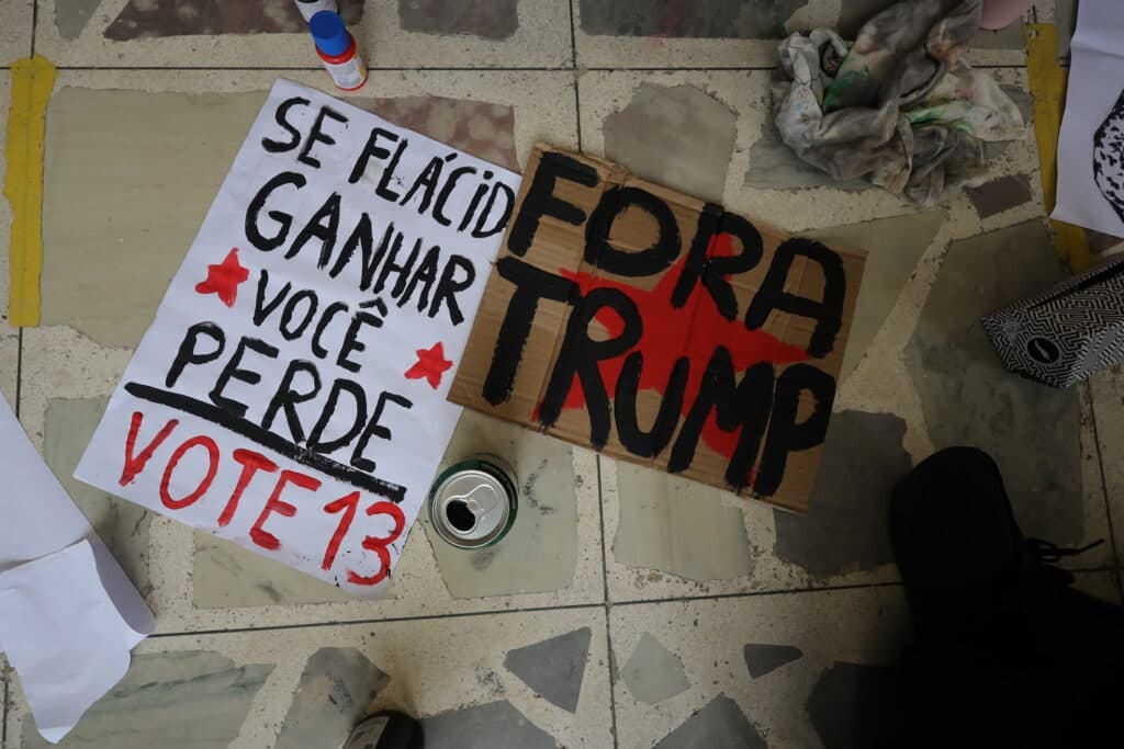 Hand-painted protest signs on tiled floor reading "Se Flacid ganhar, voce perde, Vote 13" and "Fora Trump" with paint supplies nearby Hand-painted protest signs on tiled floor reading "Se Flacid ganhar, voce perde, Vote 13" and "Fora Trump" with paint supplies nearby