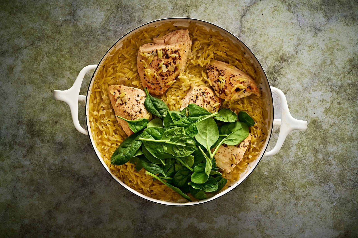 Lemon chicken orzo pasta with lemon juice and fresh spinach added to the pan, looking beautiful and bright. 