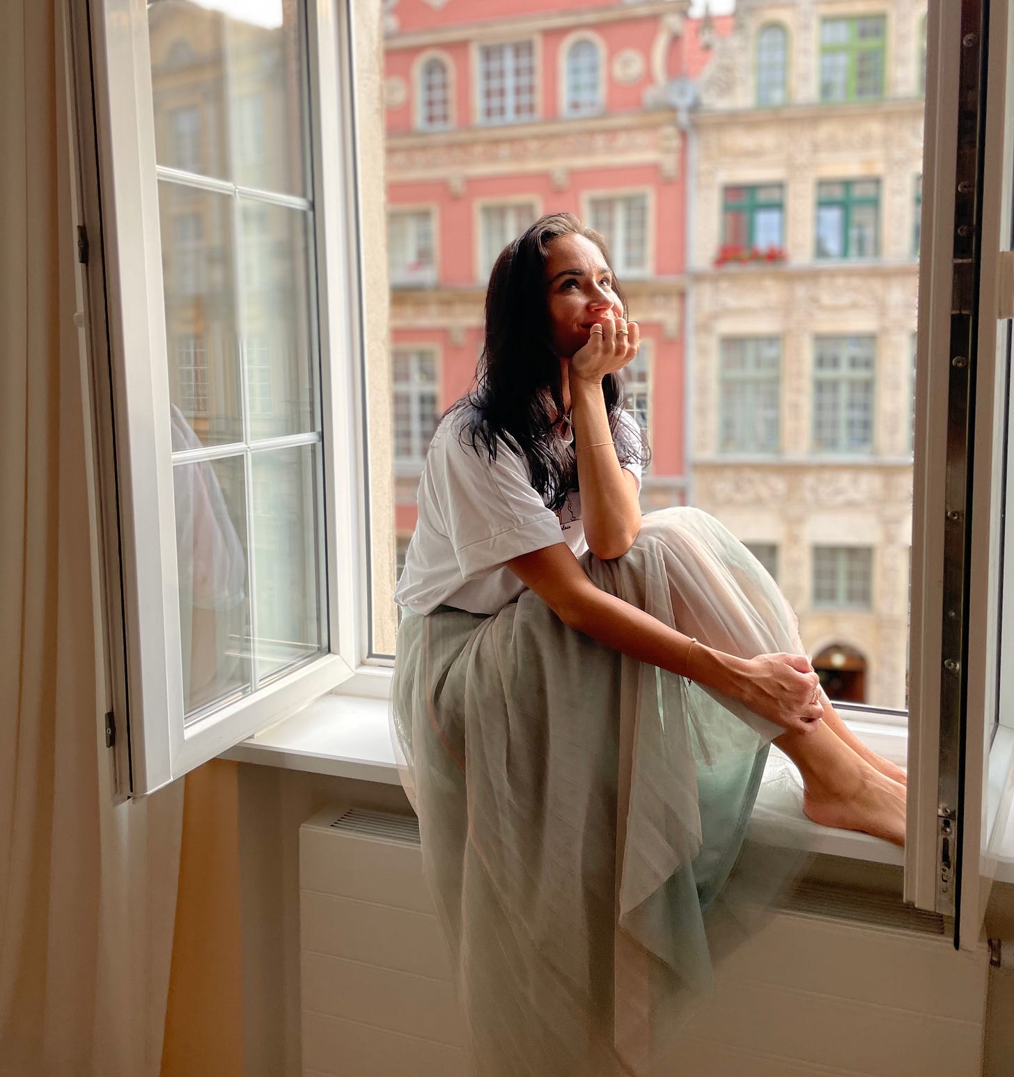 sonja matejko in white dress sitting in windowsill with hand under chin