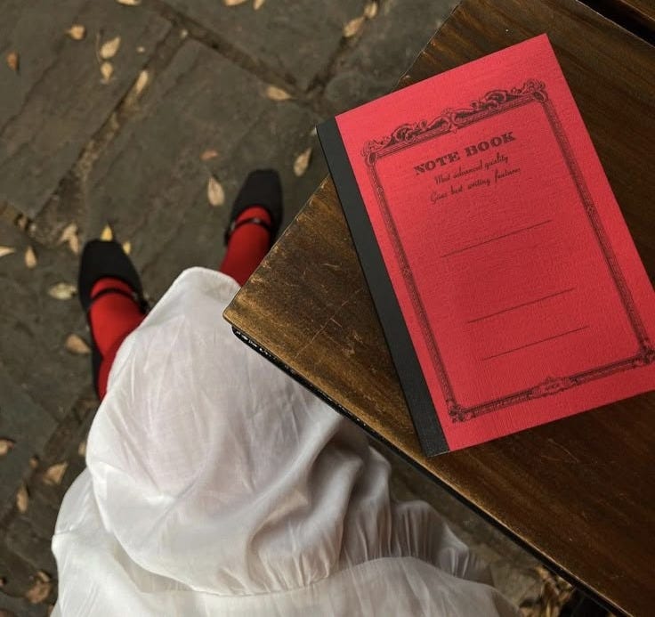 This may contain: a red book sitting on top of a wooden table next to a persons feet and legs