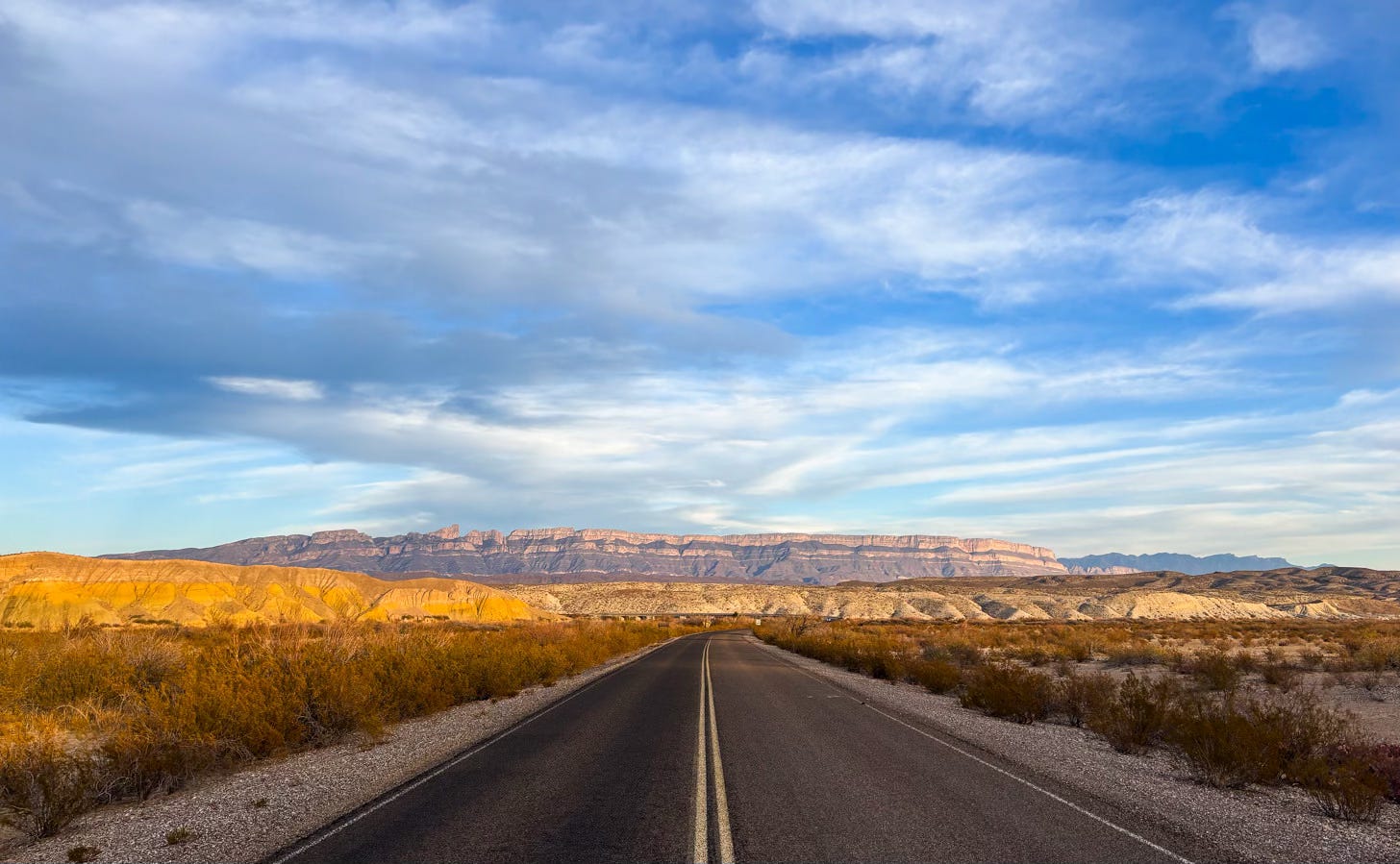 empty two lane highway going through desert toward mountains empty two lane highway going through desert toward mountains