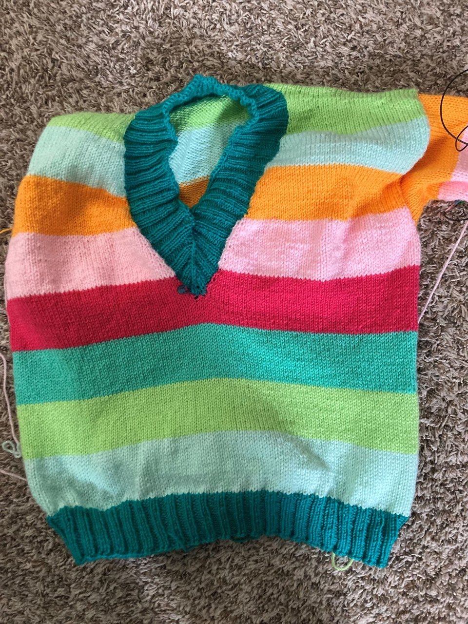 The body of a handknit sweater in bright stripes of sherberty colors with a deep turquoise ribbed v-neck.