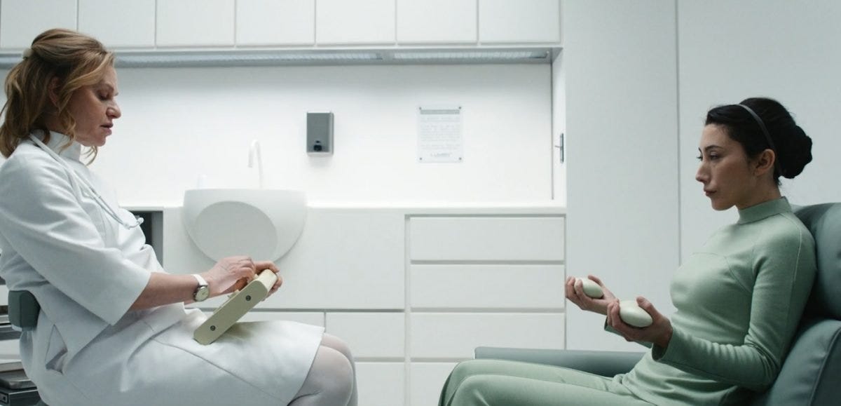 A nurse checks Gemma as she holds rocks in a white room on Severance