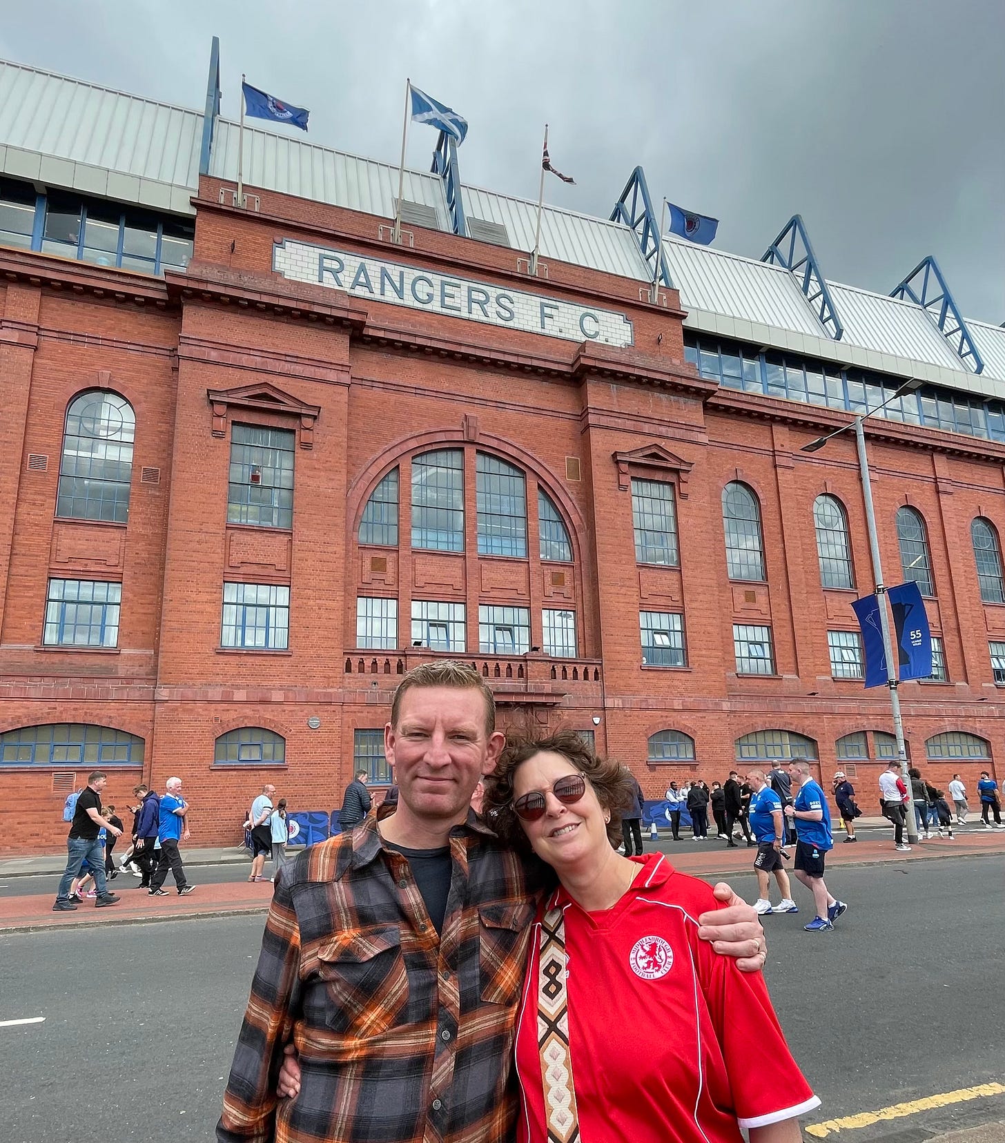 Liz and Ben standing outside the main stand of Ibrox. It's a brick built building with 'Rangers F C' picked out in tiles above the main entrance. 
