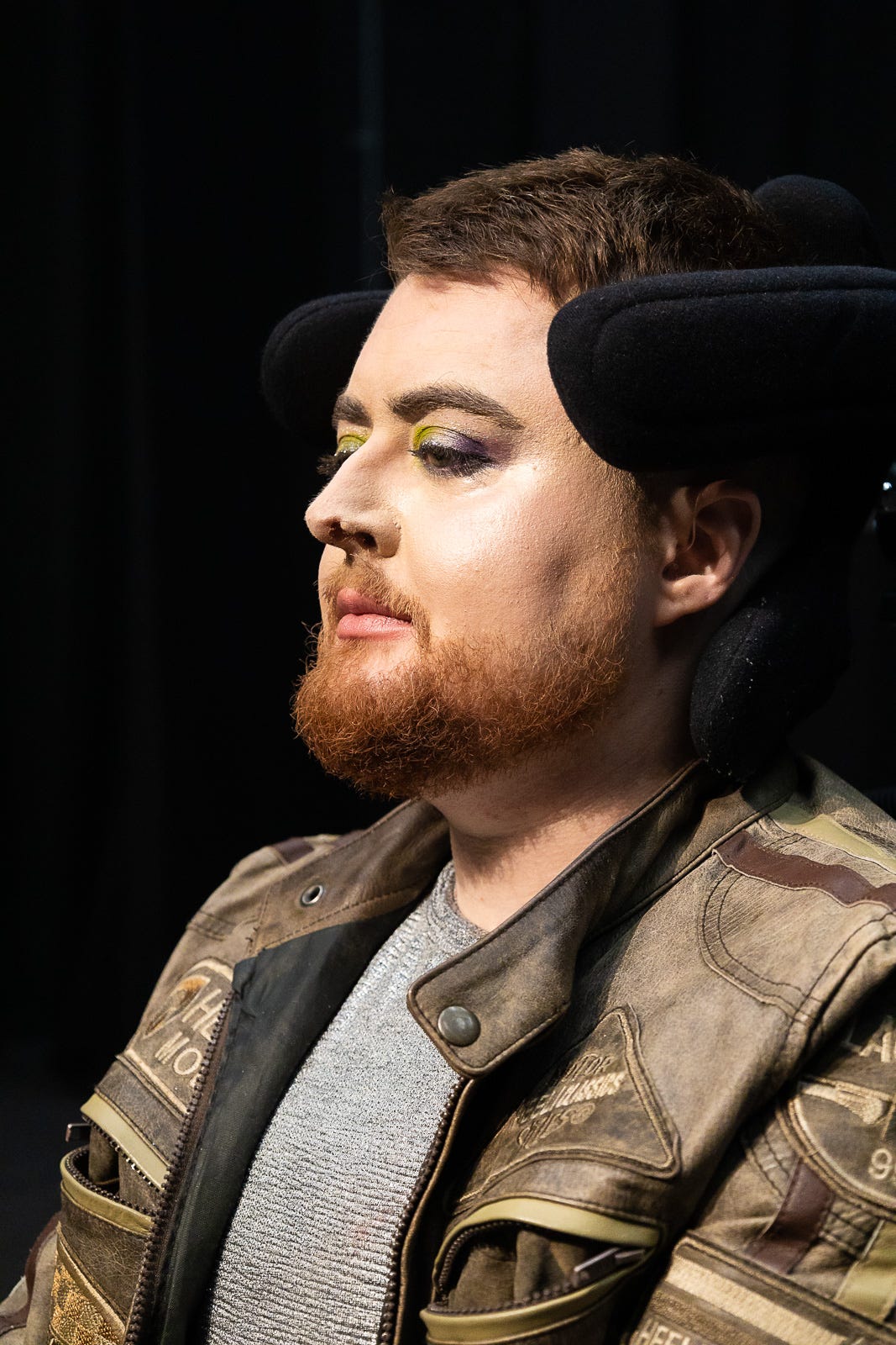 A regal image of Jamie Hale, a white electric wheelchair user, chest up, with lipstick and eyeshadow on