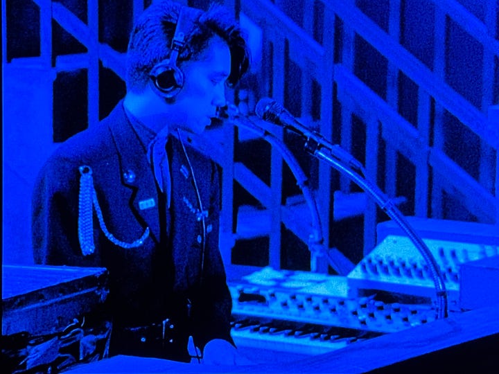 Still images from Tokyo Melody: Sakamoto in front of a large outdoor video screen, Sakamoto playing live in YMO.
