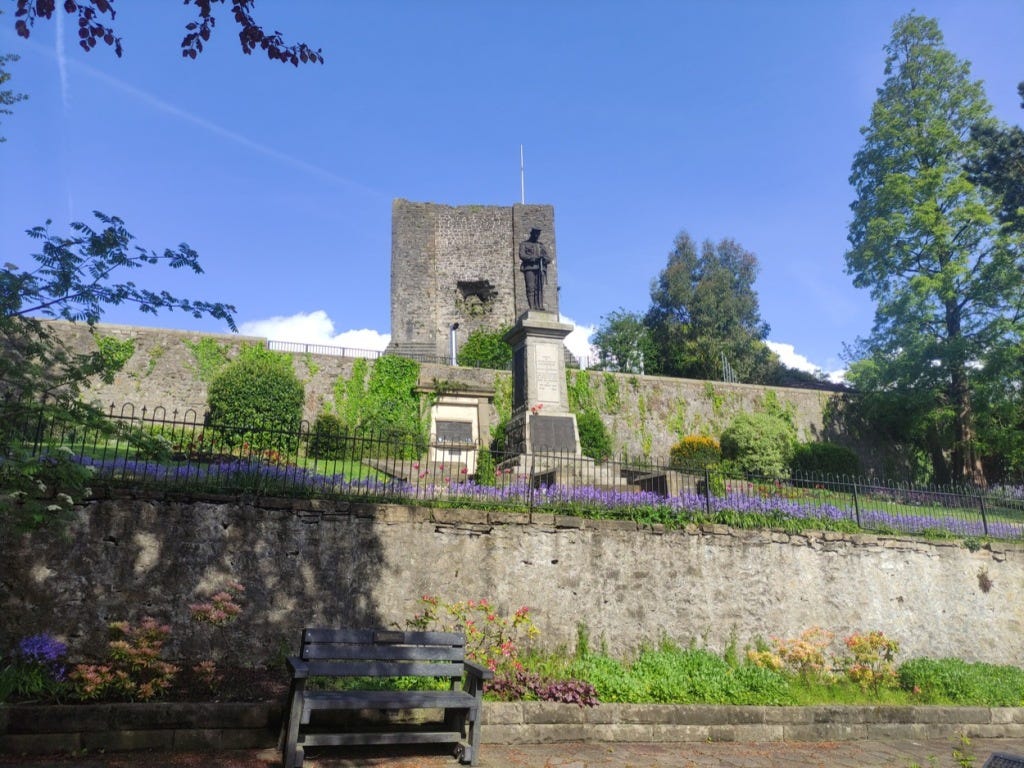 A war memorial in front of the castle keep, with a line of purple flowers all along the railings in front.