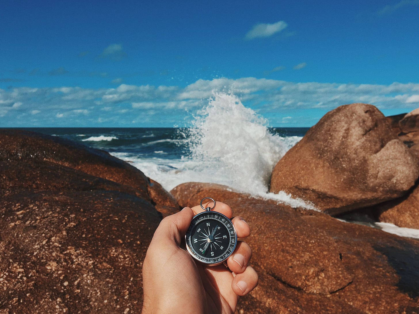 An adventurer holds a compass near the ocean's rocky shore, as waves crash dramatically An adventurer holds a compass near the ocean's rocky shore, as waves crash dramatically