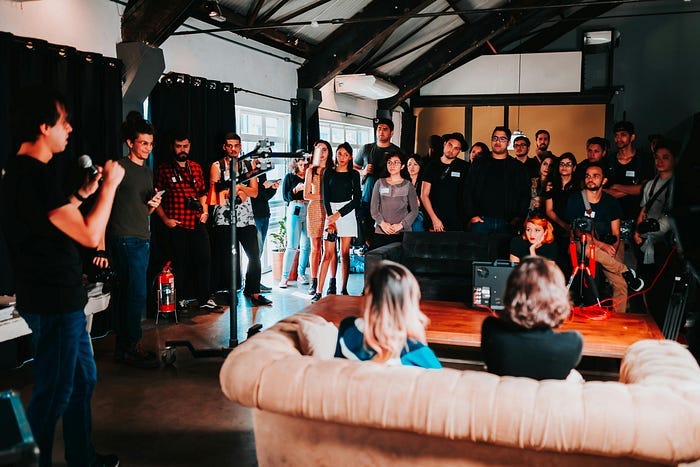 A man with a microphone addressing everyone before a performance. They’re all listening as he spells out instructions for what to do next. A man with a microphone addressing everyone before a performance. They’re all listening as he spells out instructions for what to do next.