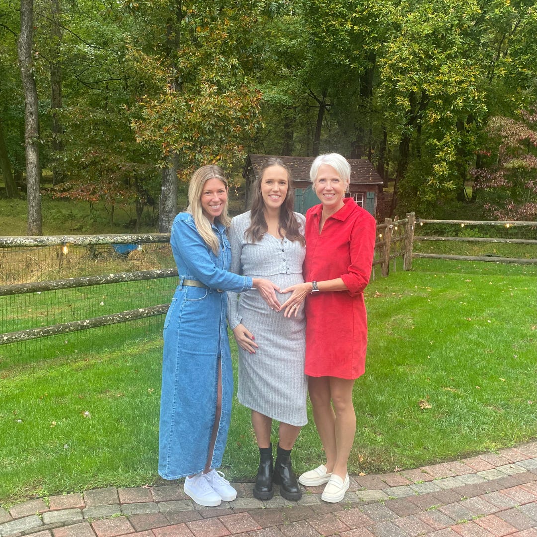 A mother and two adult daughters, one of which is pregnant, standing against the woods. A mother and two adult daughters, one of which is pregnant, standing against the woods.