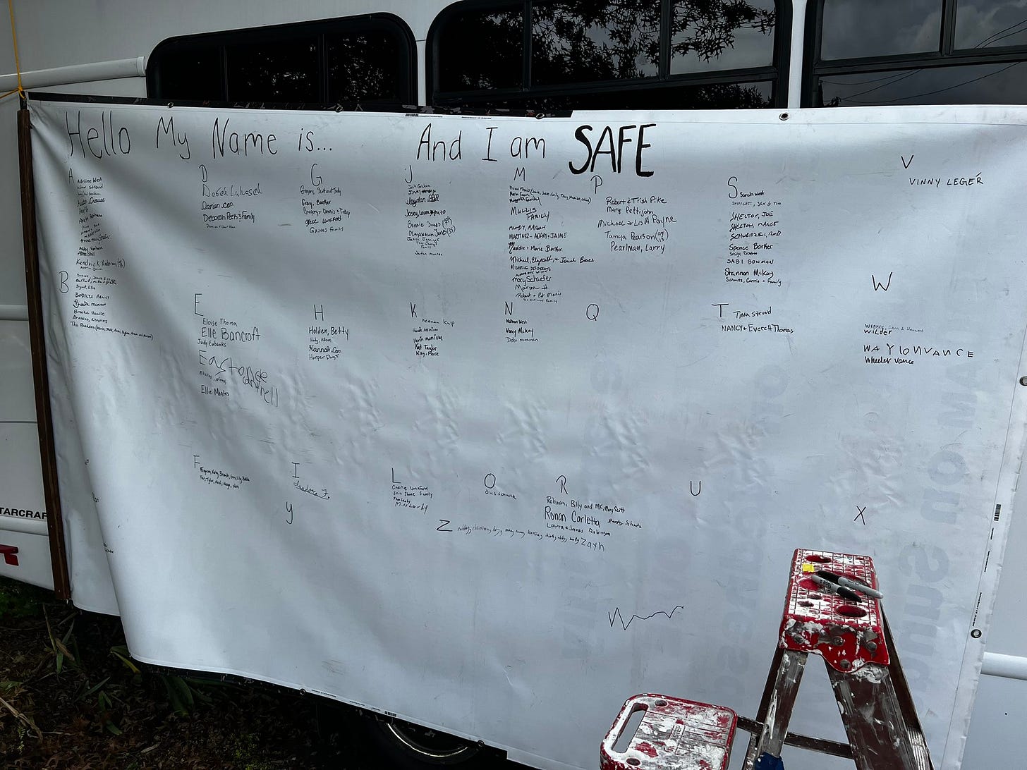 "Hello my name is... and I am safe." Sheet hanging with names written on it.