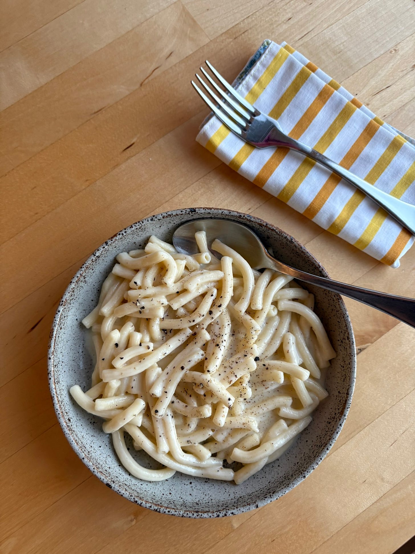 A bowl of mac and cheese made with macaroni and topped with freshly ground black pepper.