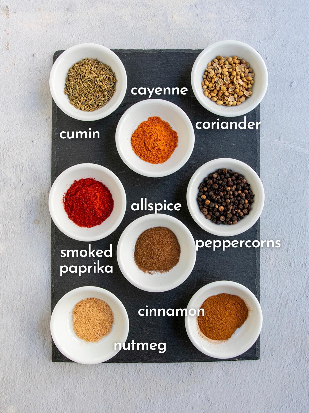 White bowls of spices on slate with each one marked with what it is.