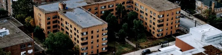A large, U-shaped apartment building made of tan brick in an urban setting as seen from above.