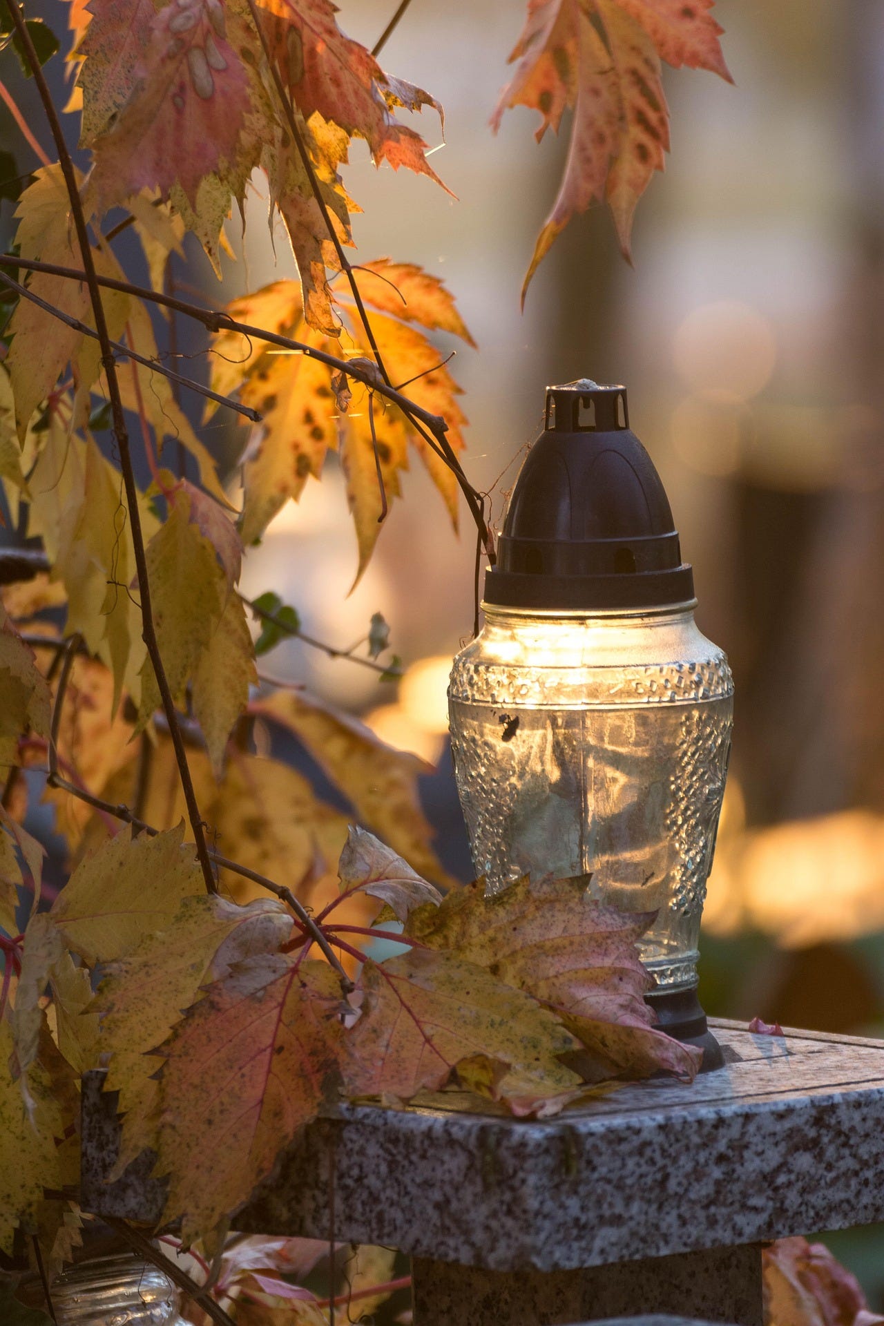 A small glass lantern lit and resting on a marble ledge, with autumn leaves hanging near it.