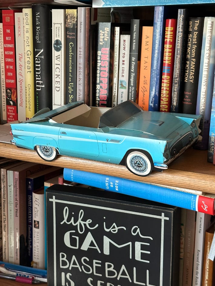 A blue paper or cardboard toy car rests on a bookshelf.