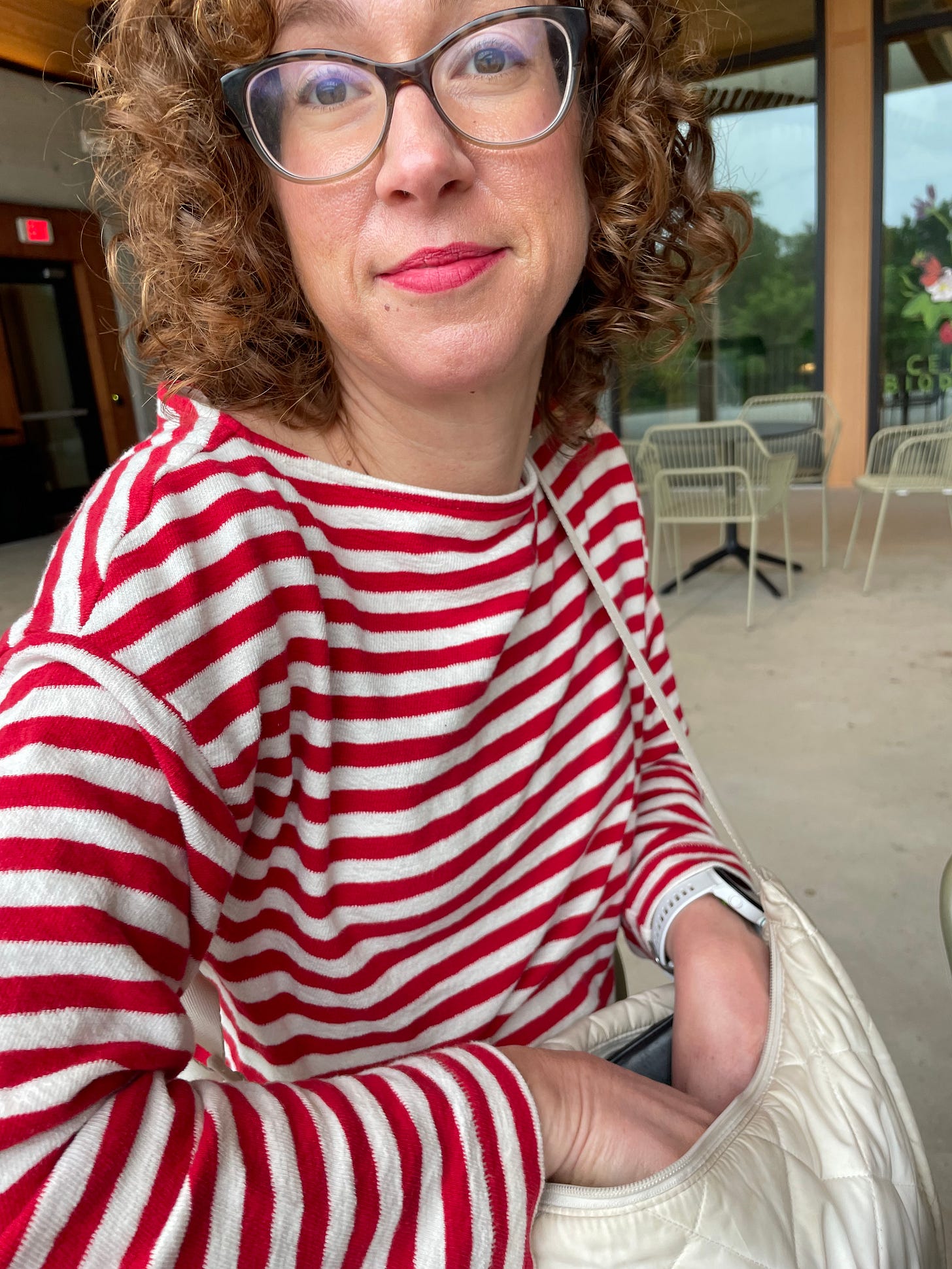 Heather Lanier stares at the camera and digs into her cream-colored purse for a tissue to help someone clean up chocolate hands or face; she wears a long-sleeved red and white striped shirt and tortoise shell glasses